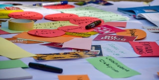 Kreative Ideen, Wünsche und Forderungen der Teilnehmenden liegen auf buntem Papier verteilt auf einem Tisch.