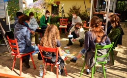 Mehrere Personen sitzen auf Stühlen in einem Kreis draußen zusammen und diskutieren.