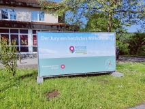 Großes Plakat vor einem Haus mit Willkommensspruch für die Jury in der Biosphäre Bliesgau.