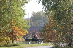 Zwei Personen auf einer Bank zwischen Bäumen, im Hintergrund eine Ziegelwand