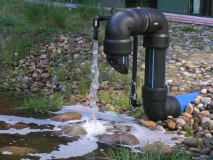 Wasser fließt aus einem Rohr in einen Teich.
