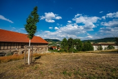  Trockener Rasen im Vordergrund, im Hintergrund ein Bauernhaus und Hügellandschaft
