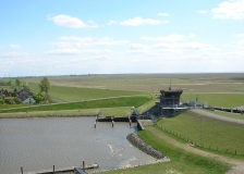 Das Foto zeigt das Sperrwerk Friedrichskoog, dass im Rugenorter Loch den Sturmflutschutz für Friedrichskoog gewährleistet. Hinter dem Hochwasserschutzteich sind die weitläufigen Salzwiesen im Wattenmeer zu sehen.