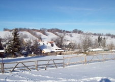 Das Foto zeigt ein Dorf im Winter. Im Hintergrund sind auf einem Hügel streifenförmig angeordnete Hecken zu sehen.