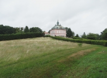 Das Foto zeigt das Fasanenschlösschen, das in der weitläufigen Parklandschaft des Schlossparks Moritzburg. Das Fasanenschlösschen ist auf einem Hügel errichtet. Zu dem Schloss führen von Hecken gesäumte Wege.
