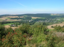 Das Foto zeigt einen weiten Blick in den Seiffener Winkel vom markanten schwartenberg auf die Gemeinde Neuhausen mit den Schloss Purschenstein. Die Landschaft ist geprägt von einem Mosaik von Wäldern, Grünland und Äckern.