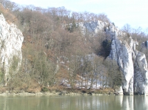 Gewaltige Felswände im Uferbereich der Donau prägen das Landschaftsbild. Der partiell bewaldete Hang wird durch eine dünne Schneedecke durchzogen.