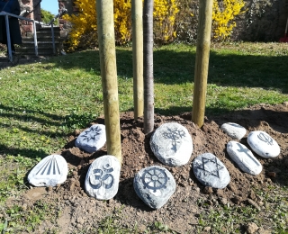 Neun Steine am mit religiösen Symbolen der beteiligten Glaubensgemeinschaften Stamm einer Linde