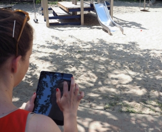 Eine Person mit einem Tablet vor einem Spielplatz.